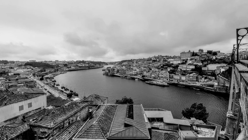 a black and white photo of a river and buildings, by Nadir Afonso, pexels contest winner, view from high, overcast gray skies, portugal, low quality footage