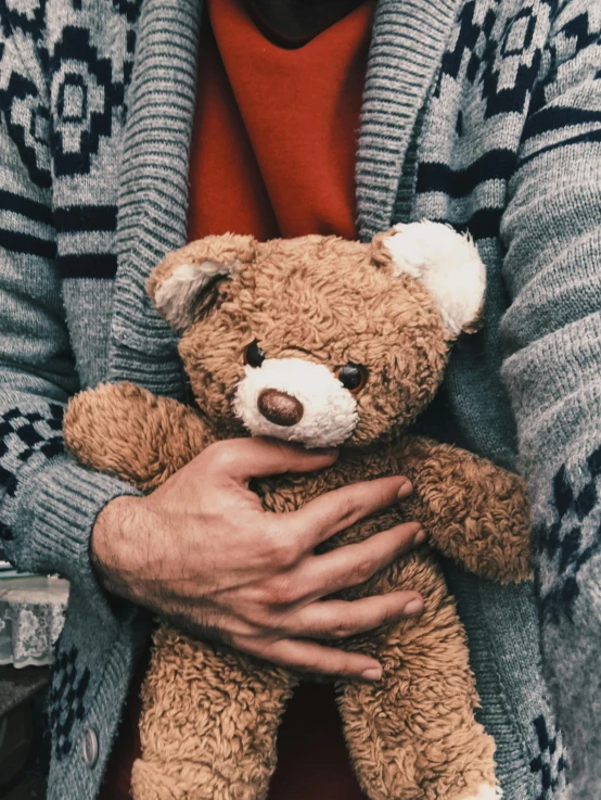 a man holding a teddy bear in his hands, by Niko Henrichon, trending on reddit, romanticism, promo image, fatherly, wearing sweater, childrens toy