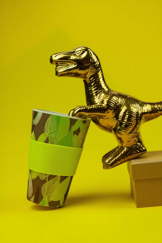 a gold dinosaur figurine next to a coffee cup, inspired by Adam Rex, jungle camo, paper cup, lime and gold hue, hero shot