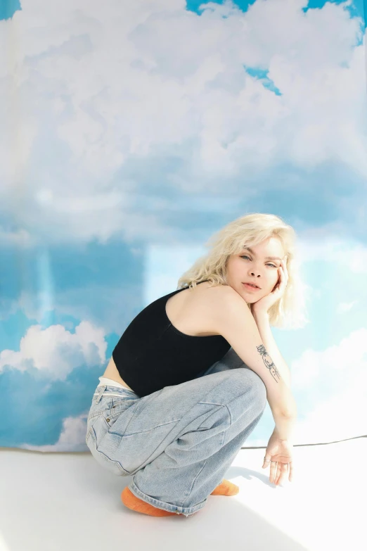 a woman sitting on top of a white surface, an album cover, inspired by Elsa Bleda, trending on pexels, cumulus cloud tattoos, platinum blonde, blue jeans, a pale skin