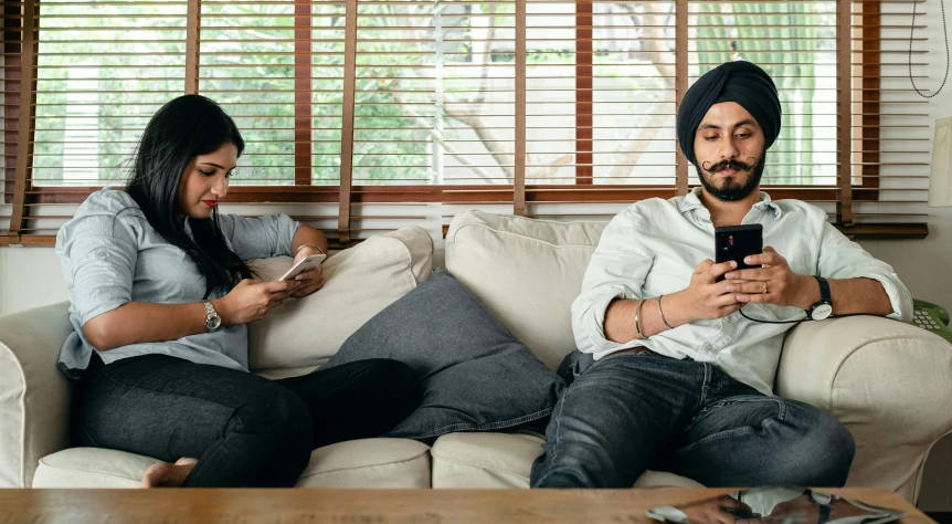 a man and a woman sitting on a couch looking at their cell phones, by Manjit Bawa, trending on pexels, renaissance, turban, two buddies sitting in a room, caring fatherly wide forehead, casual game