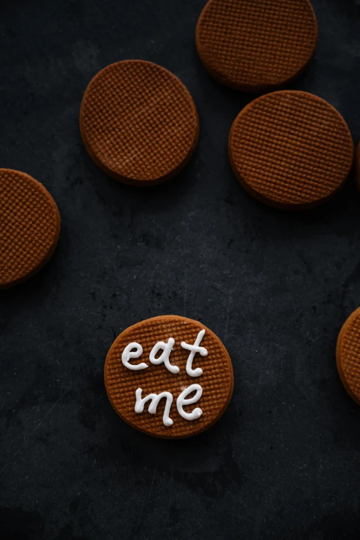 a cookie with the word eat me written on it, a picture, by Eglon van der Neer, pexels contest winner, rubber waffle outsole, on a dark background, eating cakes, thumbnail