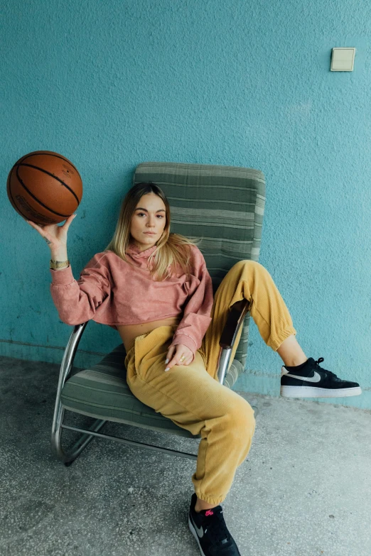 a woman sitting in a chair holding a basketball, inspired by Elsa Bleda, trending on dribble, pants, sydney sweeney, promotional image, action sports