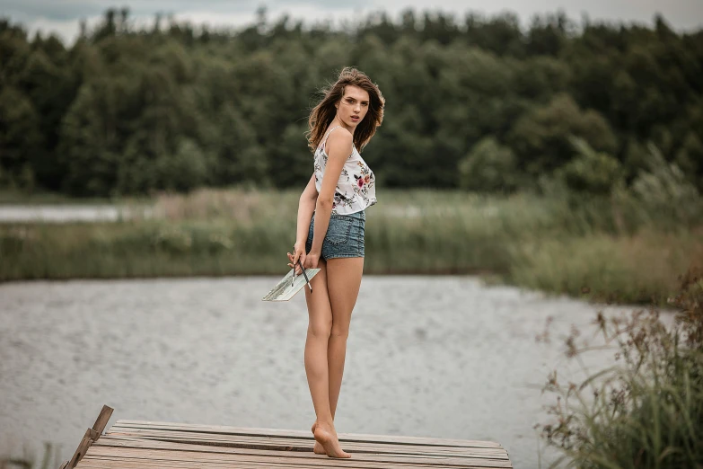 a woman standing on a dock next to a body of water, daisy dukes, ukraine. professional photo, croptop and shorts, casual pose
