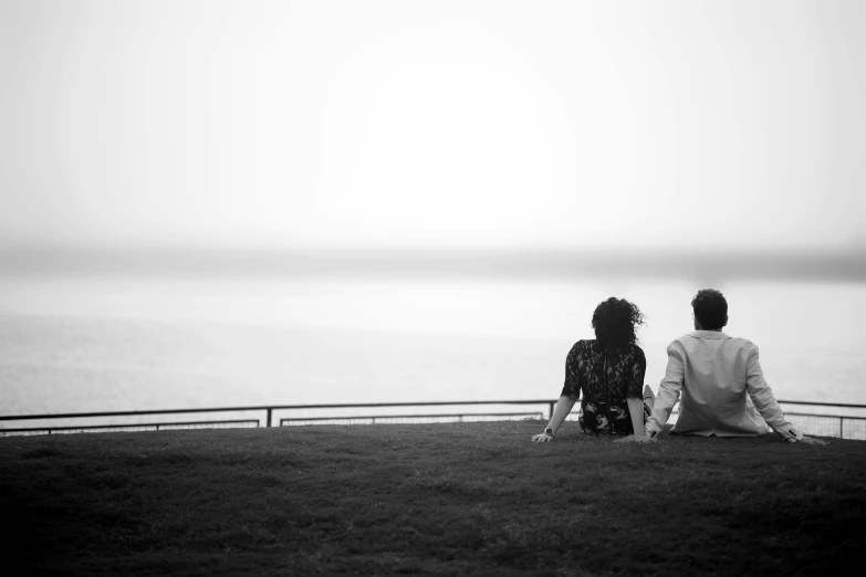 a couple of people sitting on top of a grass covered field, a black and white photo, by Daniel Gelon, unsplash, romanticism, beside the sea, rooftop romantic, hazy memory, sittin