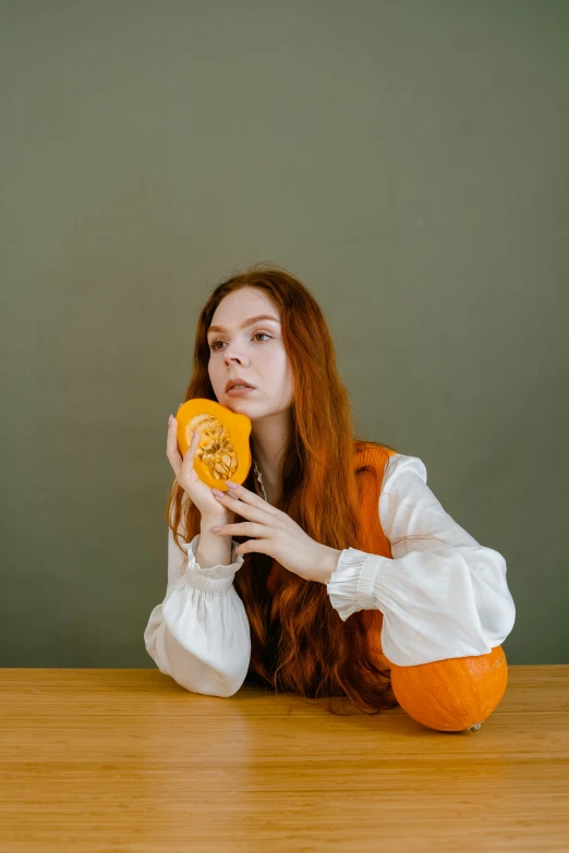 a woman sitting at a table with a donut in front of her face, an album cover, inspired by Elsa Bleda, pexels contest winner, holding a jack - o - lantern, medium long wavy ginger hair, thoughtful pose, 15081959 21121991 01012000 4k