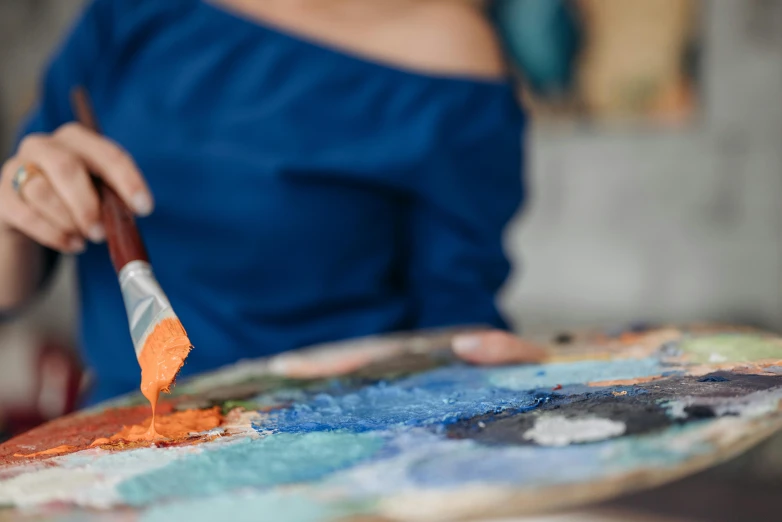 a close up of a person holding a paint brush, by Julia Pishtar, pexels contest winner, arbeitsrat für kunst, orange and blue, stands at her easel, on canvas, blue and orange