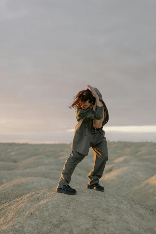 a woman standing on top of a sandy hill, an album cover, trending on pexels, wearing human air force jumpsuit, fighting stance energy, bella poarch, baggy pants