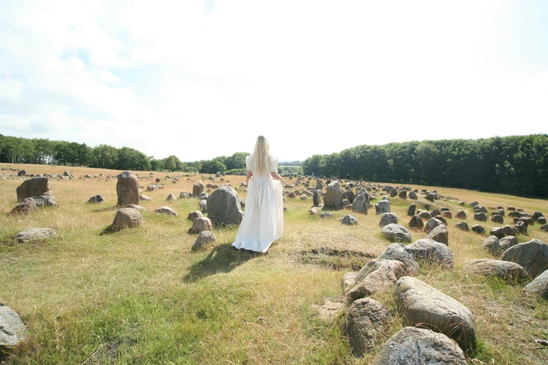 a woman in a wedding dress standing in a field of rocks, unsplash, land art, gravestones, sweden, menhirs, taken in the late 2010s