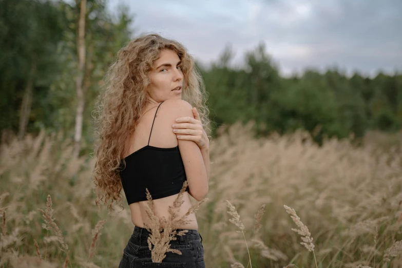 a woman standing in a field of tall grass, by Emma Andijewska, trending on pexels, renaissance, wearing a black cropped tank top, curly blonde hair | d & d, brown curly hair, attractive body