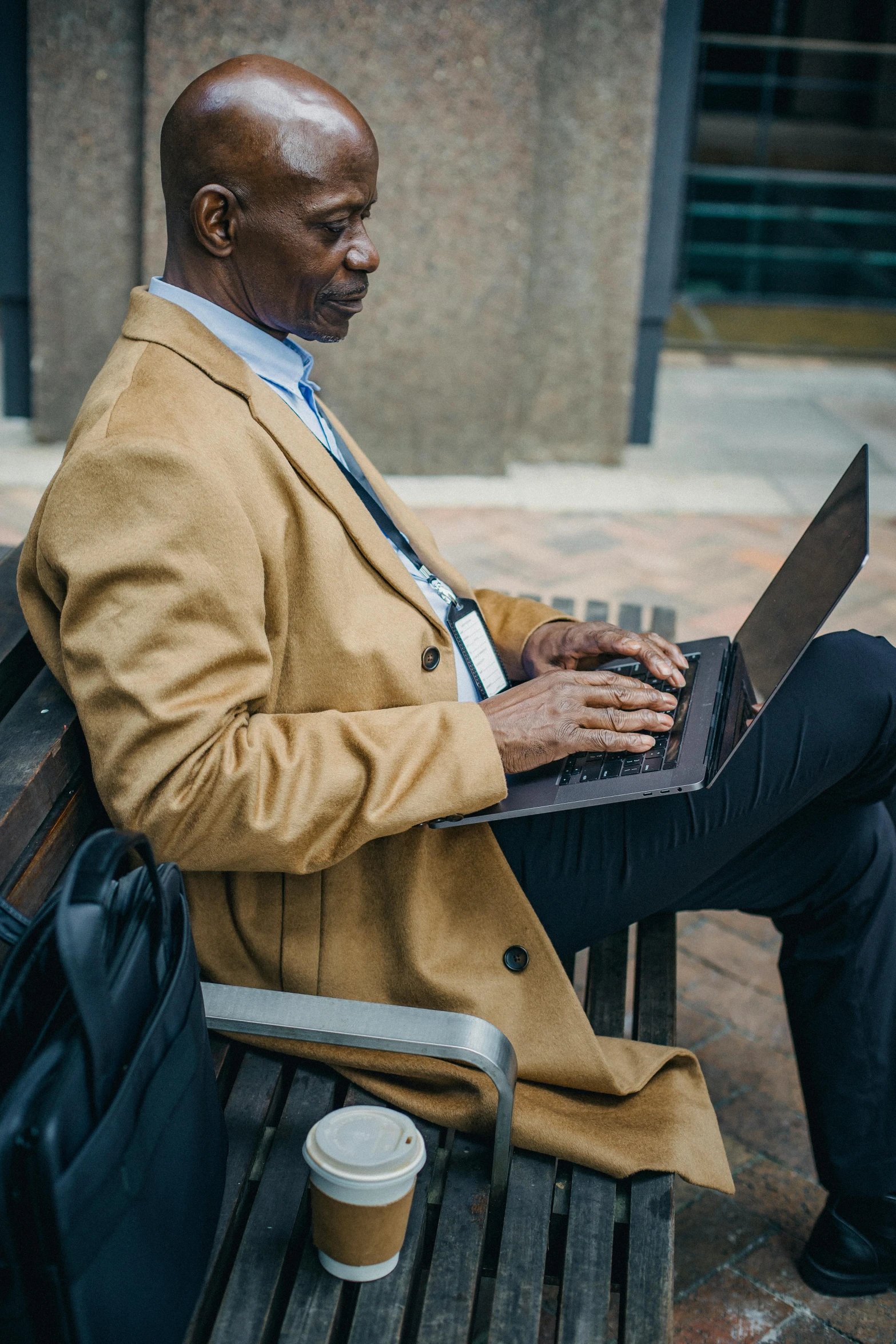 a man sitting on a bench using a laptop, trench coat and suit, dark skinned, tech robes, multiple stories