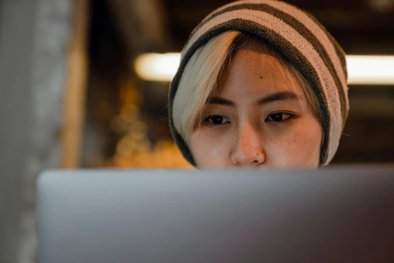 a woman sitting in front of a laptop computer, a photo, inspired by Elsa Bleda, trending on pexels, young cute wan asian face, wearing a beanie, avatar image, focused shot