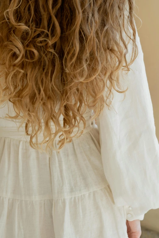 a woman with long curly hair wearing a white dress, inspired by Elsa Beskow, trending on pexels, linen, detail shot, bedhead, long sleeves