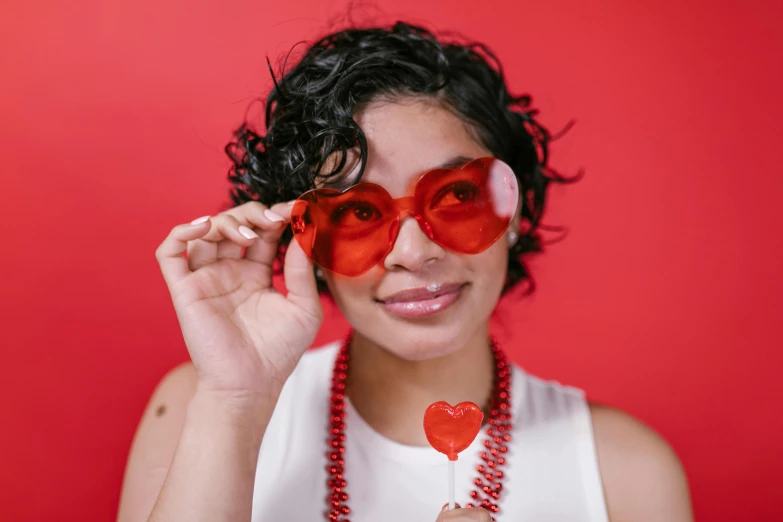 a woman holding a heart shaped lollipop lollipop lollipop lollipop lollipop lollipop lollipop lo, an album cover, by Nicolette Macnamara, pexels, pop art, small square glasses, his one yes glow red, photo booth, tessa thompson