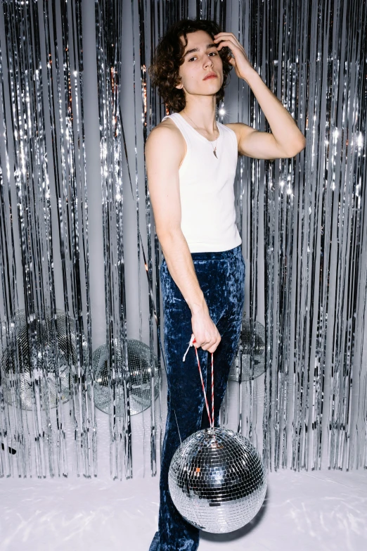 a woman standing in front of a disco ball, by Julia Pishtar, wearing : tanktop, joe keery, blue pants, bag over the waist