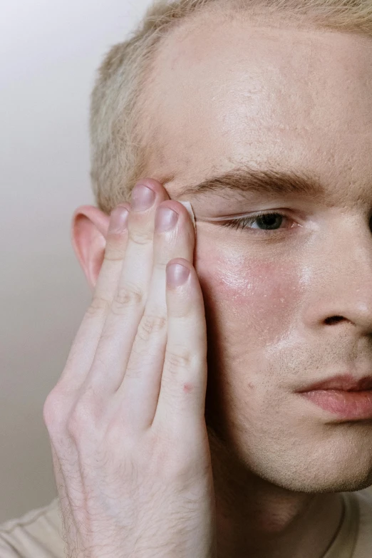 a close up of a person touching their eye, by Adam Marczyński, lean man with light tan skin, freckled pale skin, silicone skin, skincare