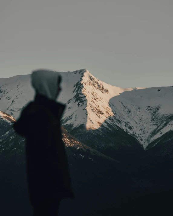 a person standing in front of a mountain, covered with snow, in the evening, wearing hoods, trending photo