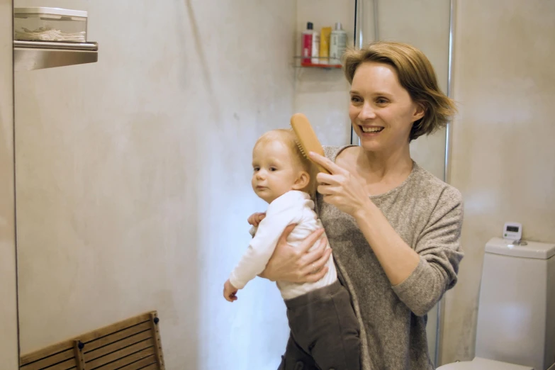 a woman holding a baby in a bathroom, by Emma Andijewska, happening, holding a wooden staff, clean hair, profile image