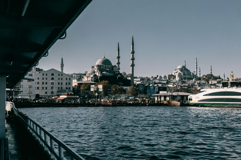 a boat on a body of water with a city in the background, a colorized photo, pexels contest winner, hurufiyya, black domes and spires, view from the sea, 🚿🗝📝, blue toned