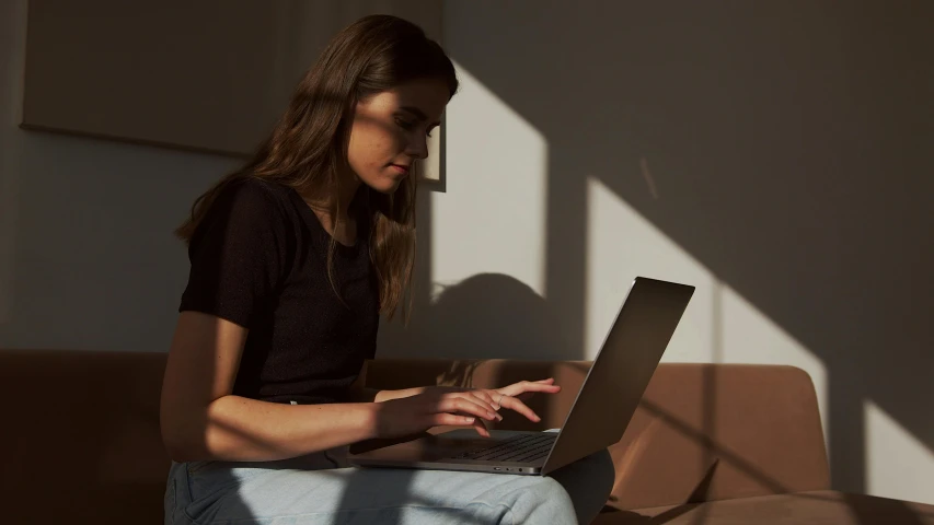a woman sitting on a couch using a laptop computer, trending on pexels, glowing light and shadow, avatar image, profile image, neutral lighting