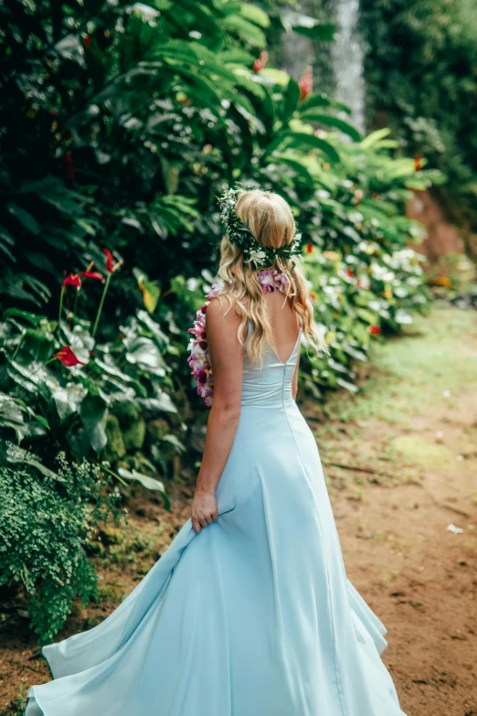 a woman in a blue dress walking down a path, unsplash, kauai springtime, romantic gown, lush garden surroundings, back