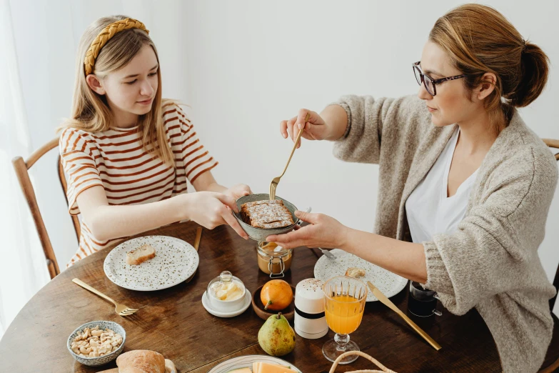 two women sitting at a table with plates of food, by Julia Pishtar, trending on pexels, maple syrup, with a kid, presenting wares, manuka