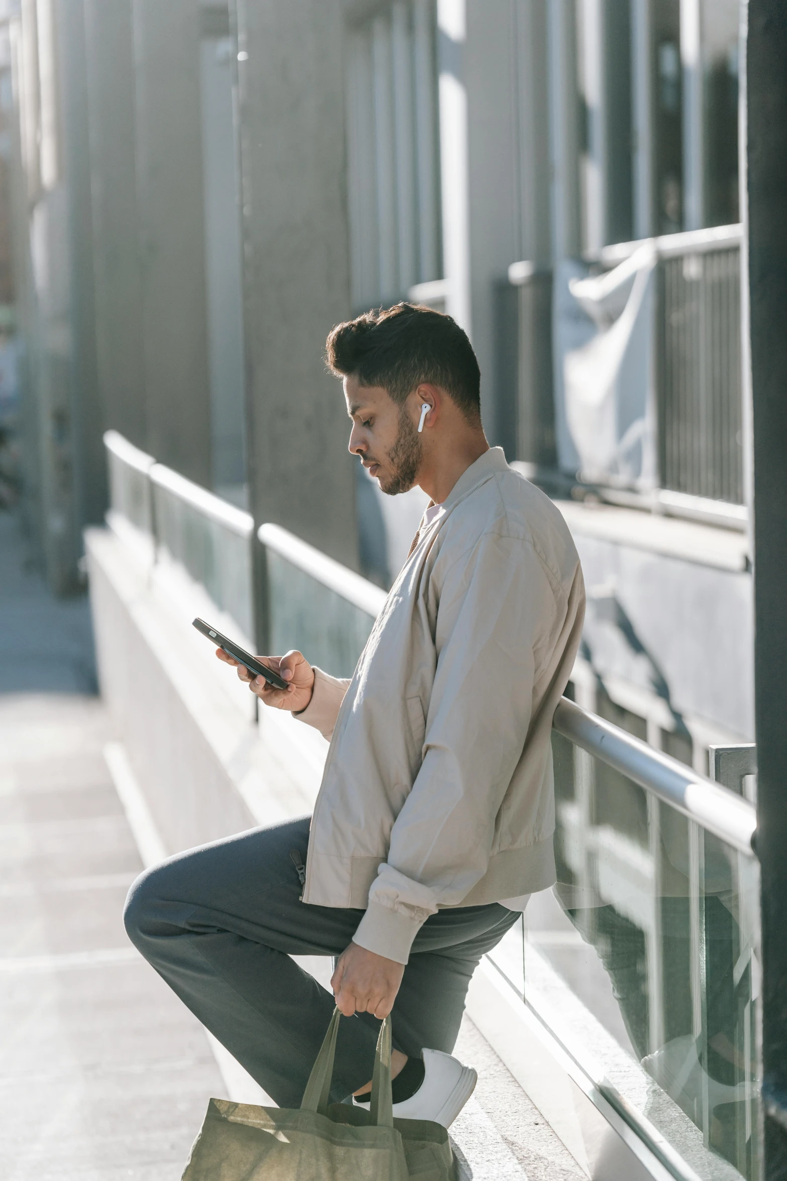 a man sitting on a ledge looking at his cell phone, trending on pexels, wearing modern headphone, grayish, standing, lean man with light tan skin