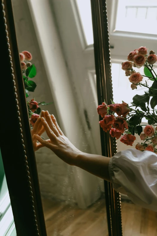 a woman reaching for flowers in front of a mirror, inspired by Elsa Bleda, roses, mid-shot