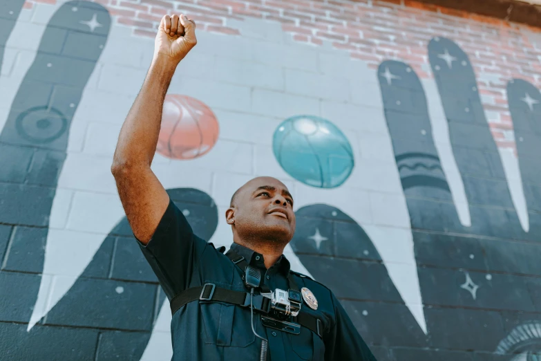 a police officer standing in front of a mural, pexels contest winner, black arts movement, 3 5 mm pointing up, holding a ball, unsplash photo contest winner, pictured from the shoulders up