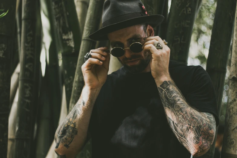 a man with tattoos talking on a cell phone, pexels contest winner, tipping his fedora, dark shades, arm tattoos, amongst foliage