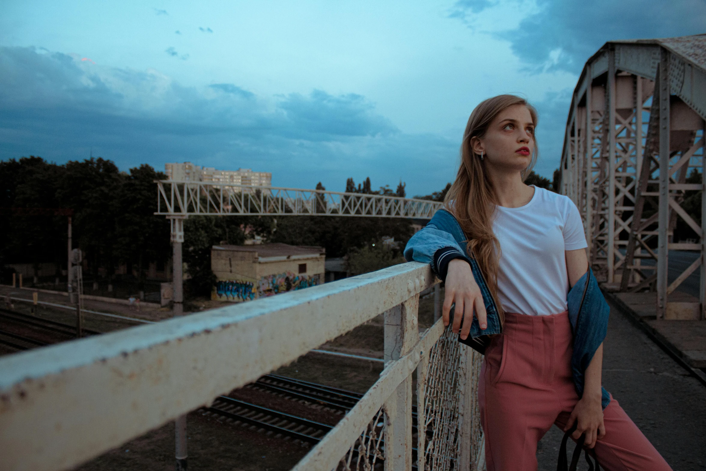 a beautiful young woman standing on top of a bridge, inspired by Elsa Bleda, pexels contest winner, graffiti, medium shot of two characters, ukraine. professional photo, early evening, thoughtful pose