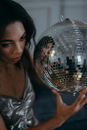 a woman holding a disco ball in her hands, an album cover, by Julia Pishtar, trending on pexels, wearing silver dress, looking into a mirror, seductive expression, **cinematic