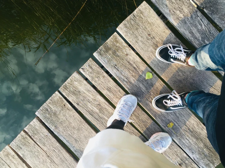 a person standing on a dock next to a body of water, sneaker, walking together, top - down photograph, instagram picture