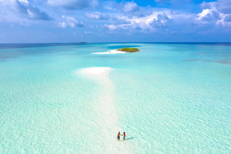 a couple of people that are standing in the water, pexels contest winner, hurufiyya, maldives in background, birds eye, pastels colours, white sand