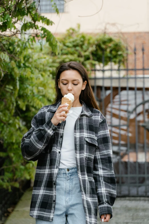 a woman standing on a sidewalk eating an ice cream cone, trending on unsplash, wearing plaid shirt, model wears a puffer jacket, 1 6 years old, 15081959 21121991 01012000 4k