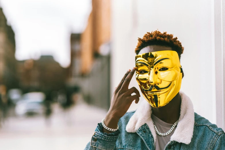 a man with a mask on talking on a cell phone, trending on pexels, afrofuturism, a boy made out of gold, anonymous lion face, ashteroth, revolutionary