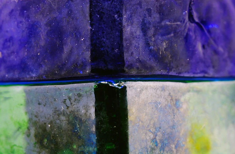 a close up of a bottle on a table, inspired by Mordecai Ardon, unsplash, lyrical abstraction, blue and purple and green, panels, ultramarine metal, yellow purple green black