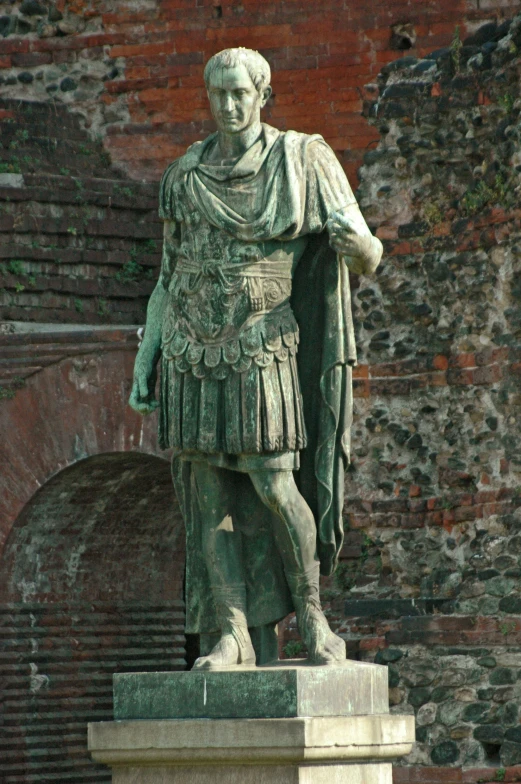 a statue of a roman soldier in front of a brick wall, wearing a toga and sandals, monuments, general human form, smirking