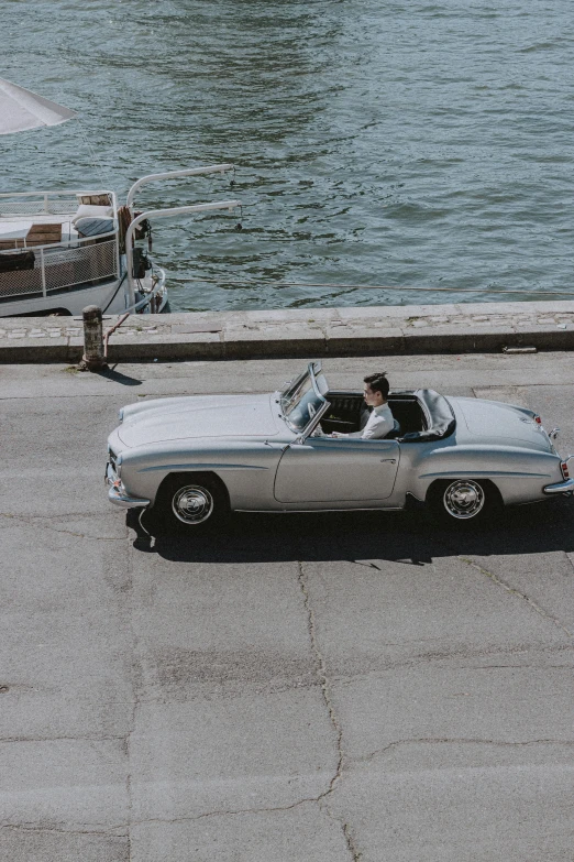 a white car driving down a street next to a body of water, by Carlo Martini, pexels contest winner, doing an elegant pose, soft top, 15081959 21121991 01012000 4k, grey