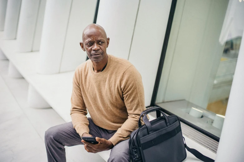 a man sitting on a bench holding a cell phone, holding a gold bag, sitting in front of computer, thumbnail, portrait image