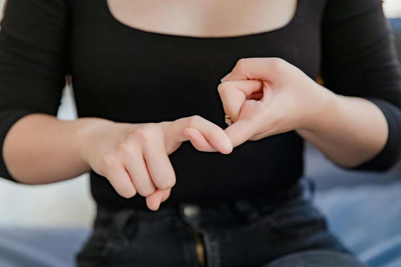 a woman sitting on a bed making a heart with her hands, trending on pexels, stick poke, with index finger, wearing a black shirt, rectangle