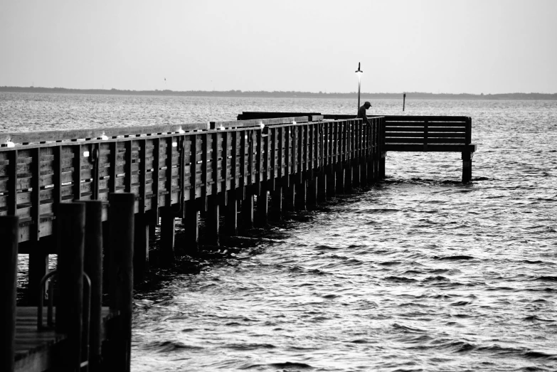 a black and white photo of a pier, fishing, pondering, slightly pixelated, single figure