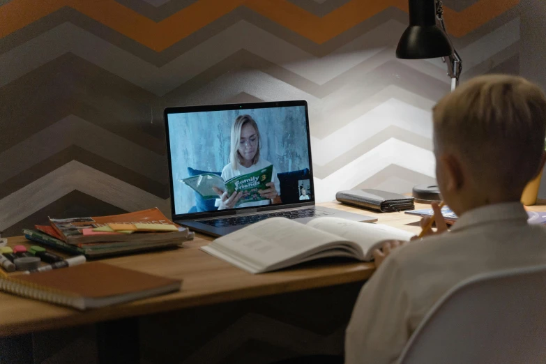 a young boy sitting at a desk in front of a laptop computer, by Julia Pishtar, pexels, figuration libre, still image from tv series, reading a book, long distance shot, a blond