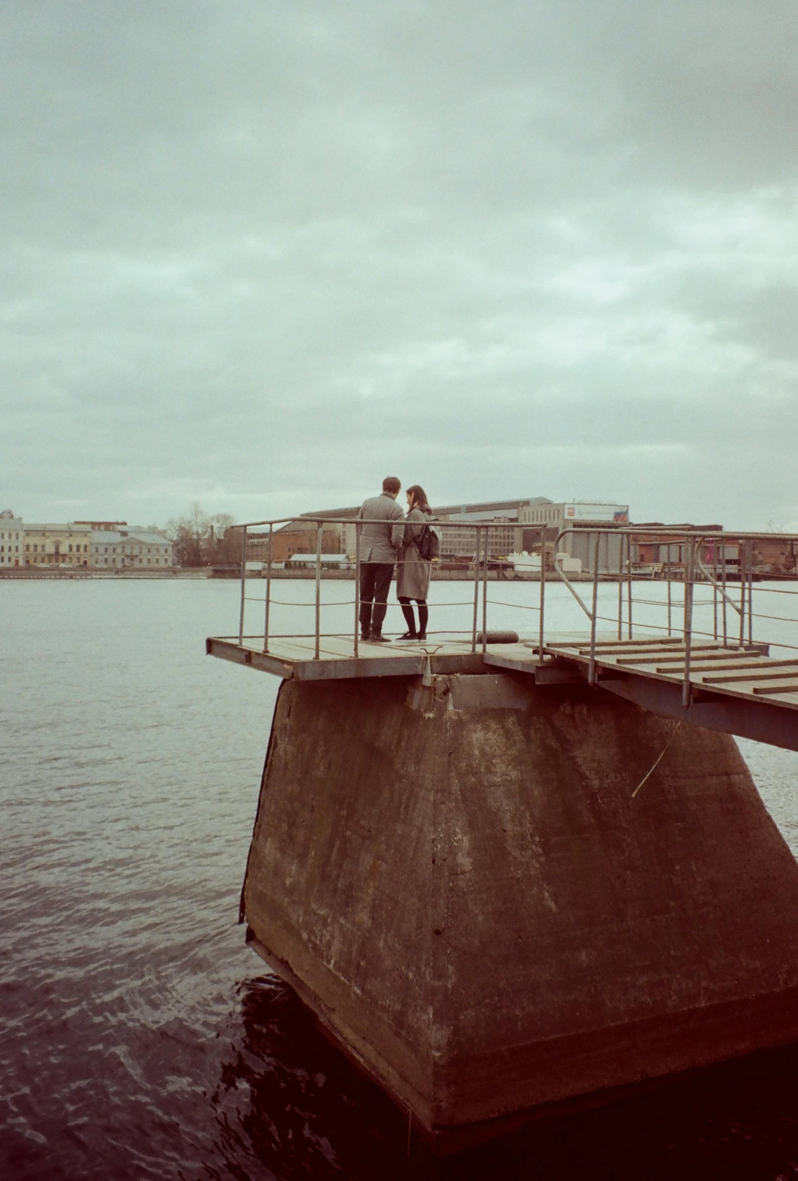 a couple standing on a pier next to a body of water, by Christen Dalsgaard, happening, berghain, helsinki, on a birdge, low quality photo