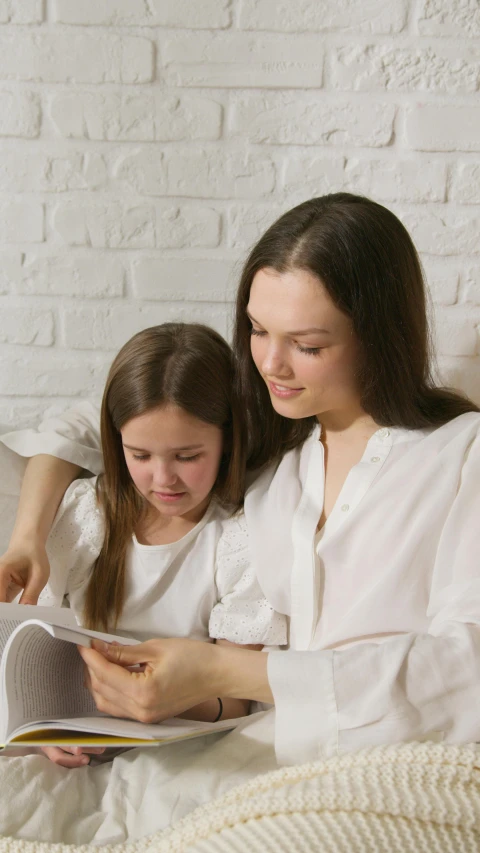 a mother and daughter reading a book on a bed, a cartoon, pexels, wearing white clothes, programming, low quality photo, schools