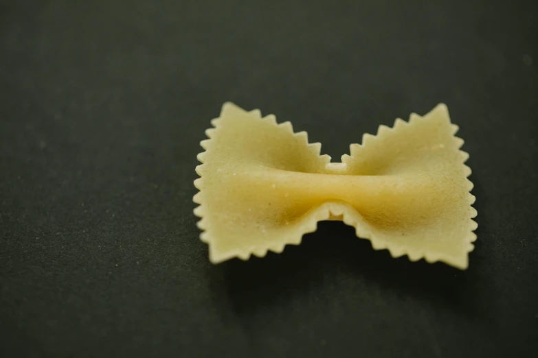 a close up of a pasta bow on a black surface, by Adam Marczyński, pexels contest winner, on a pale background, tiny mouth, geometrically realistic, male and female