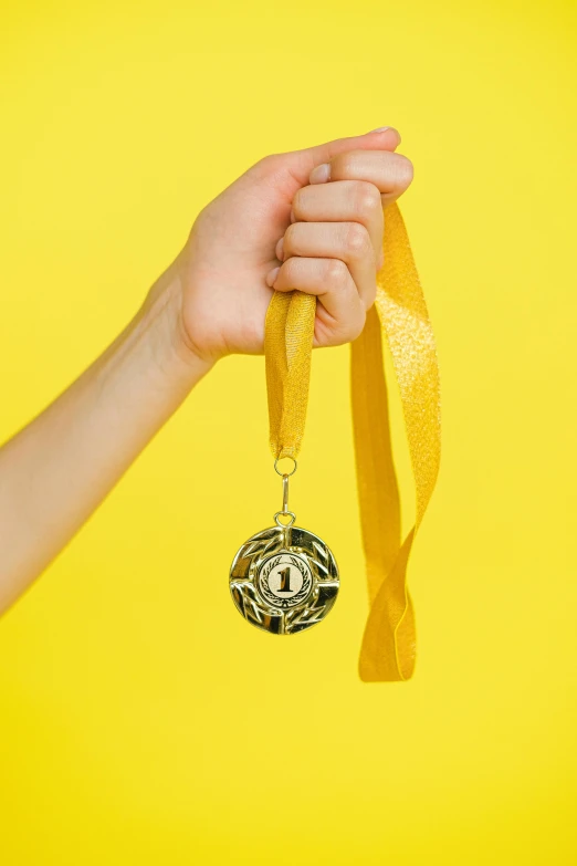 a person holding a gold medal in their hand, pexels contest winner, on a yellow canva, ribbons, adorable design, award winning advertising