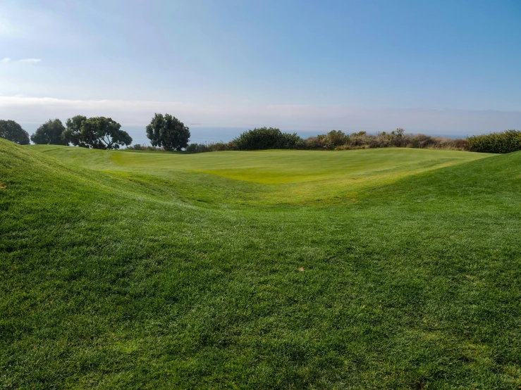 a green golf course with the ocean in the background, inspired by Dennis Miller Bunker, unsplash, malibu canyon, open field, seen from below, panorama