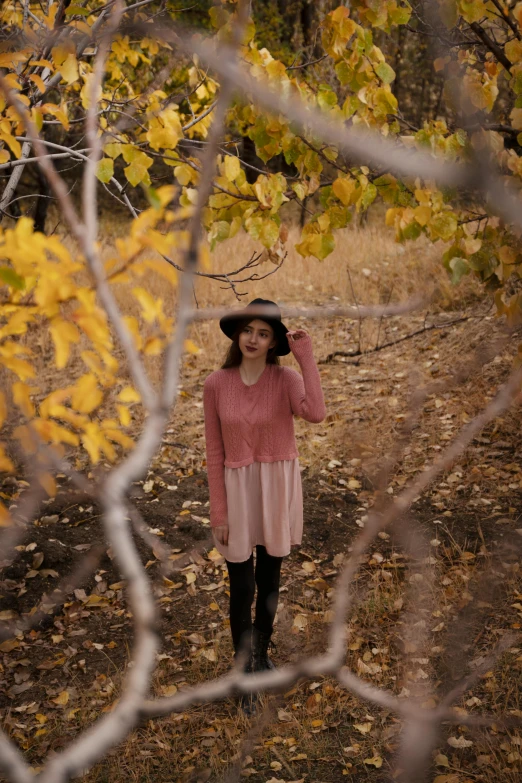 a woman in a hat is walking through the woods, a picture, unsplash, brown and pink color scheme, pose 4 of 1 6, mid fall, low quality photo