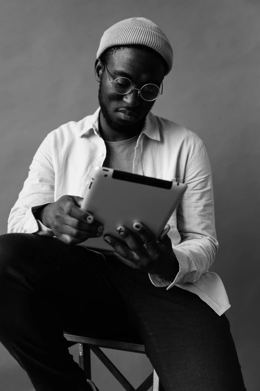 a man sitting on a chair using a tablet, by Stokely Webster, dark grey skin, nerdy, black + white, antoine-jean gr